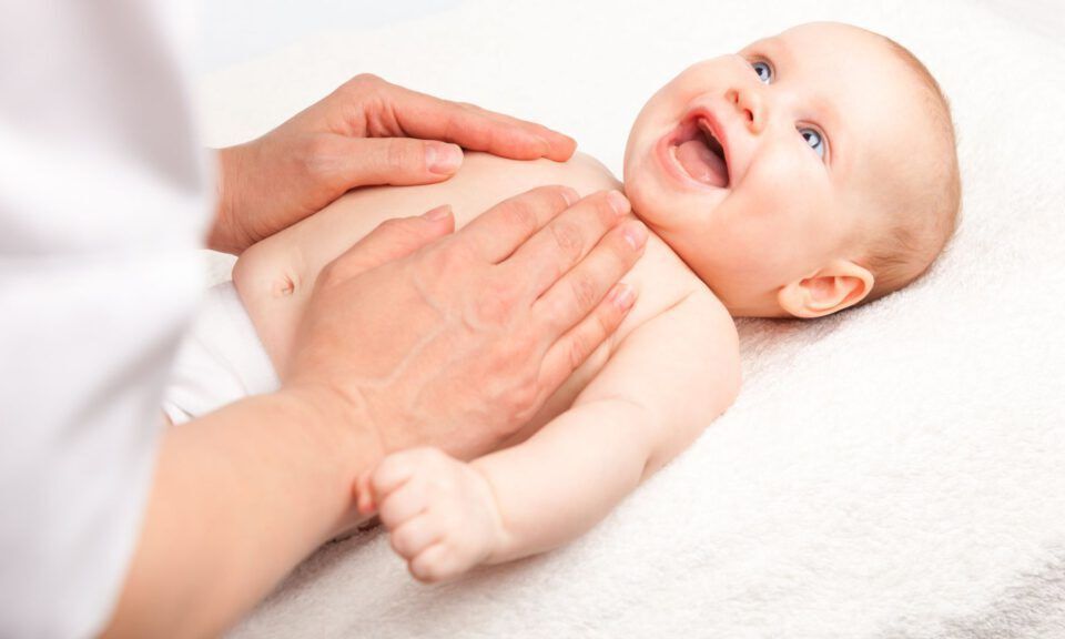 Babyssage mit zwei Händen - lachendes Baby bekommt Brustmassage